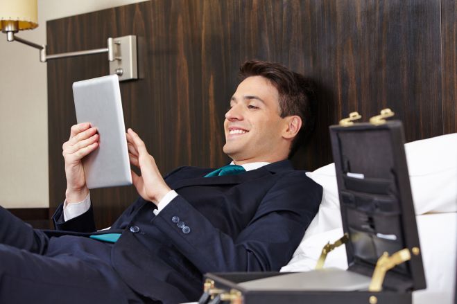 Erfolgreicher Manager liegt mit Tablet PC im Hotel auf dem Bett